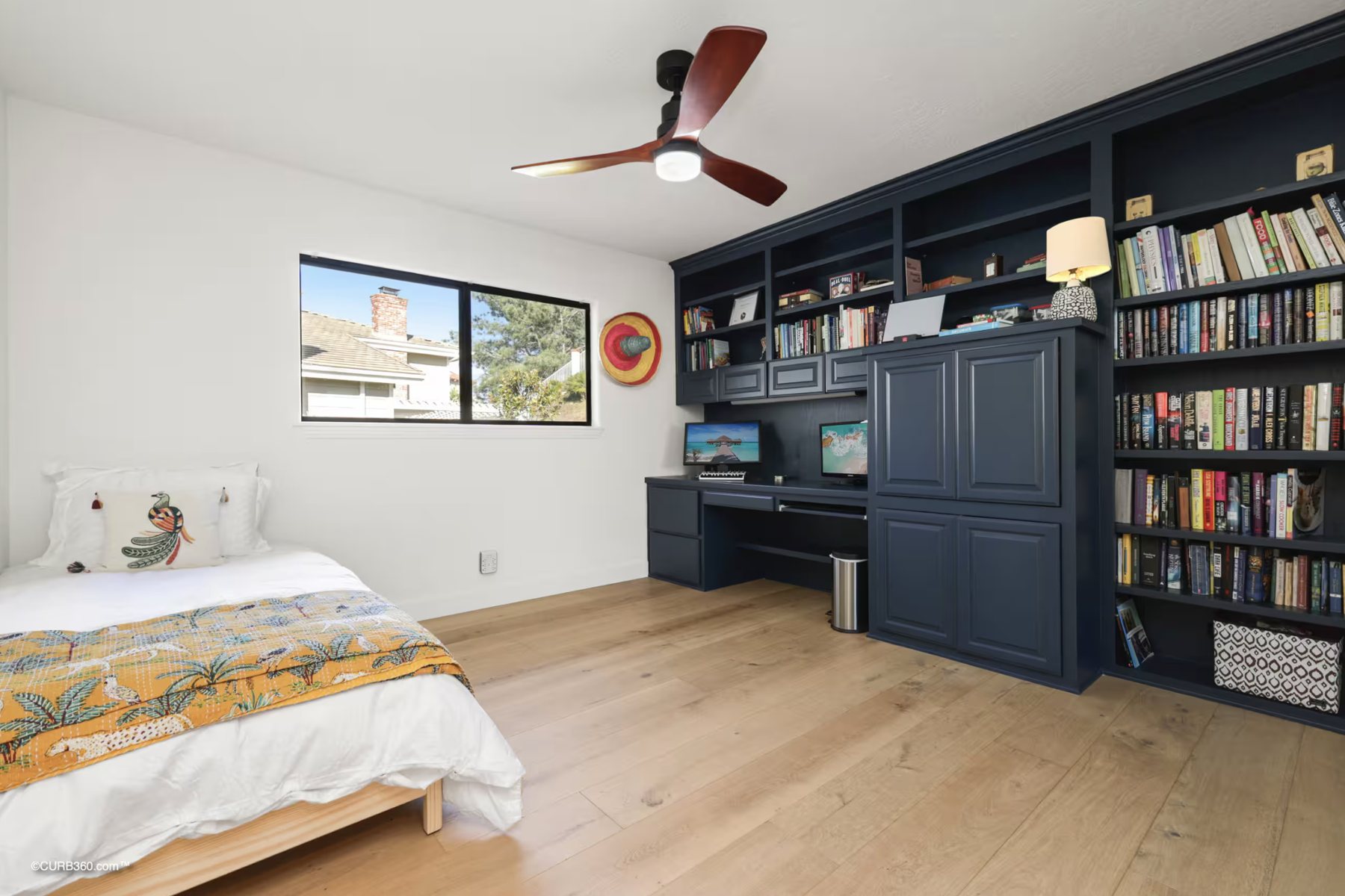 A bedroom with a bed, a large window and built-in bookshelves and desk