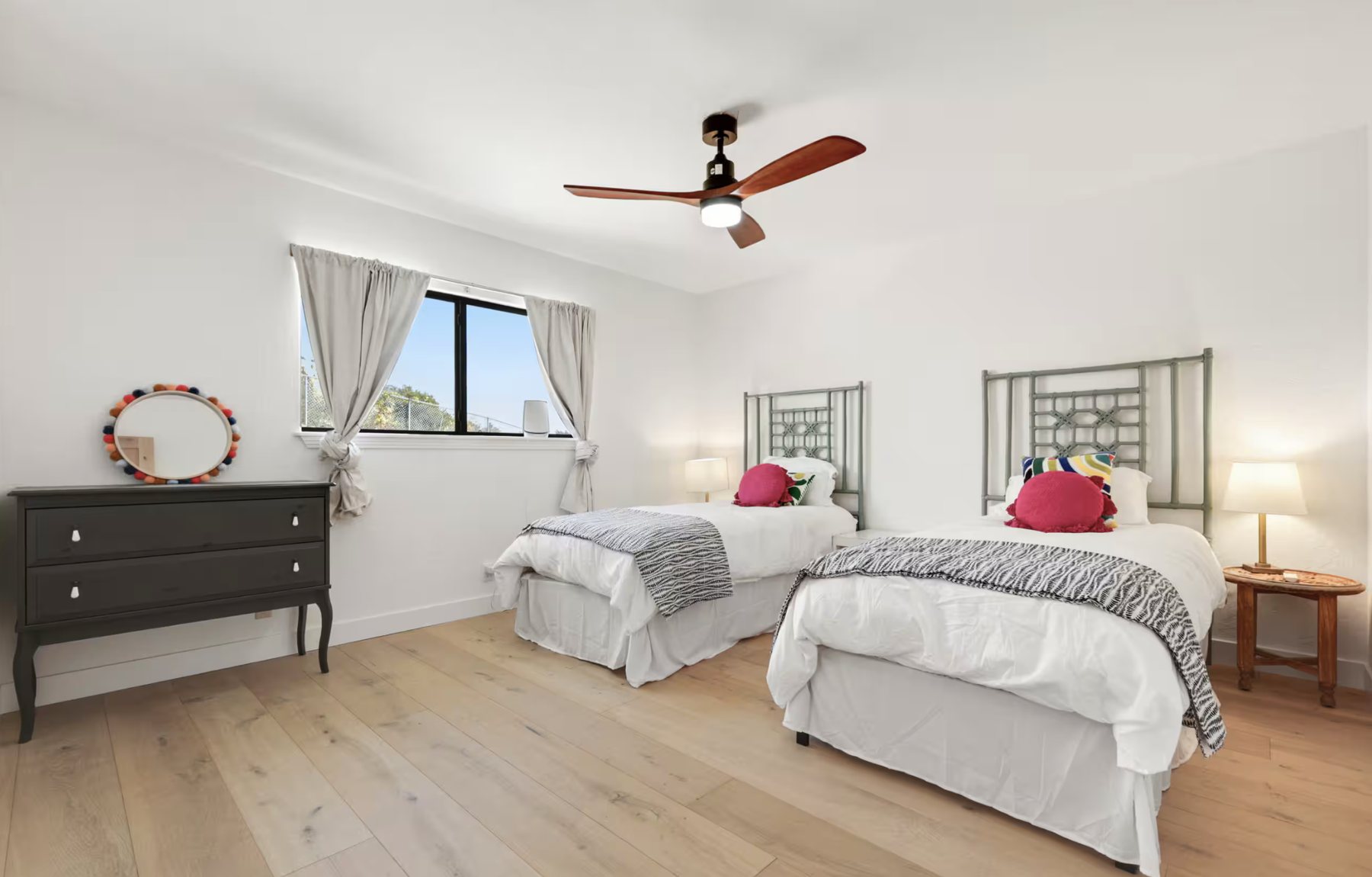 A bedroom with two twin beds with colorful pillows, a dresser and a window