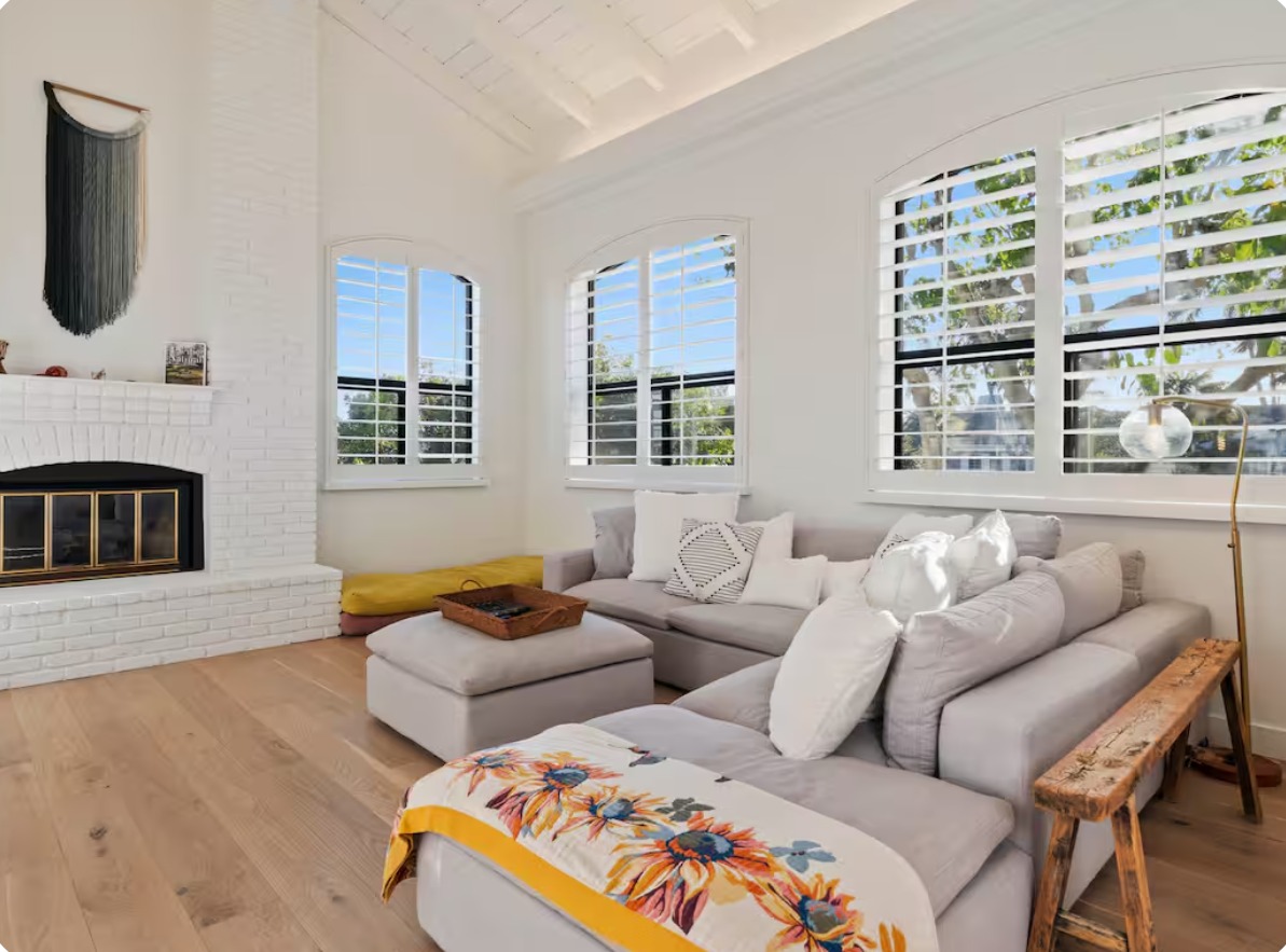 A bright living room with a soft sectional sofa, a white brick fireplace, arched windows and a vaulted ceiling